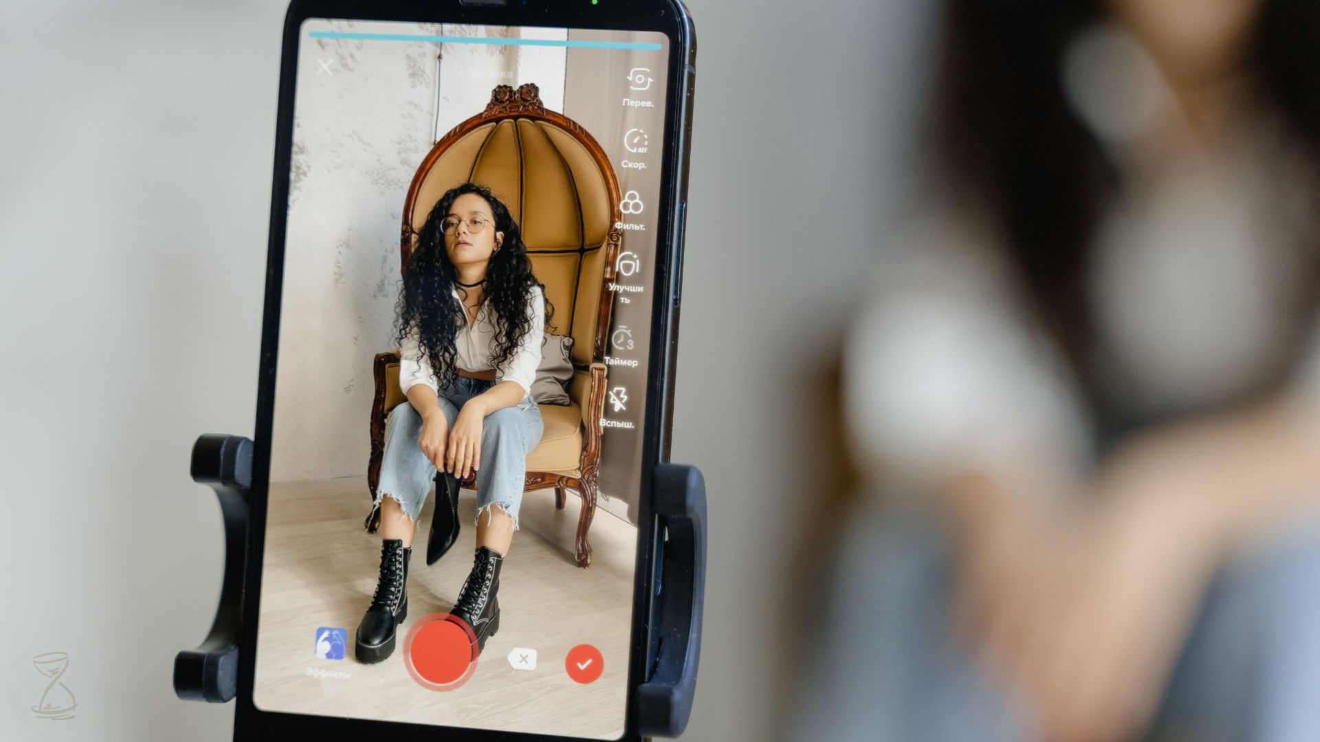 A Close-Up Shot of a Smartphone Recording a Woman Sitting on a Chair